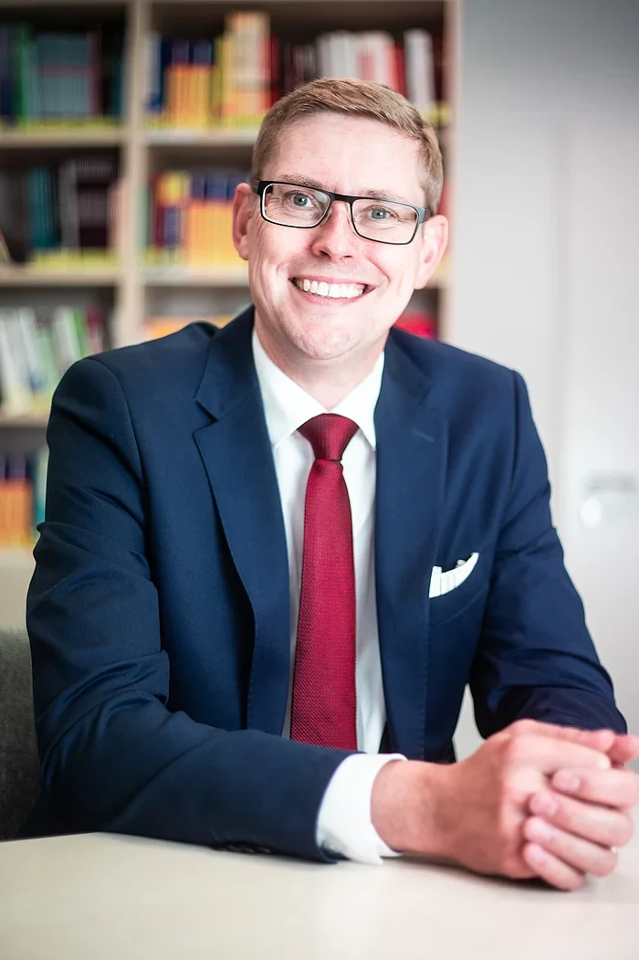 Eine Wissenschaftlerin und ein Wissenschaftler arbeiten hinter einer Glasfassade und mischen Chemikalien mit Großgeräten.